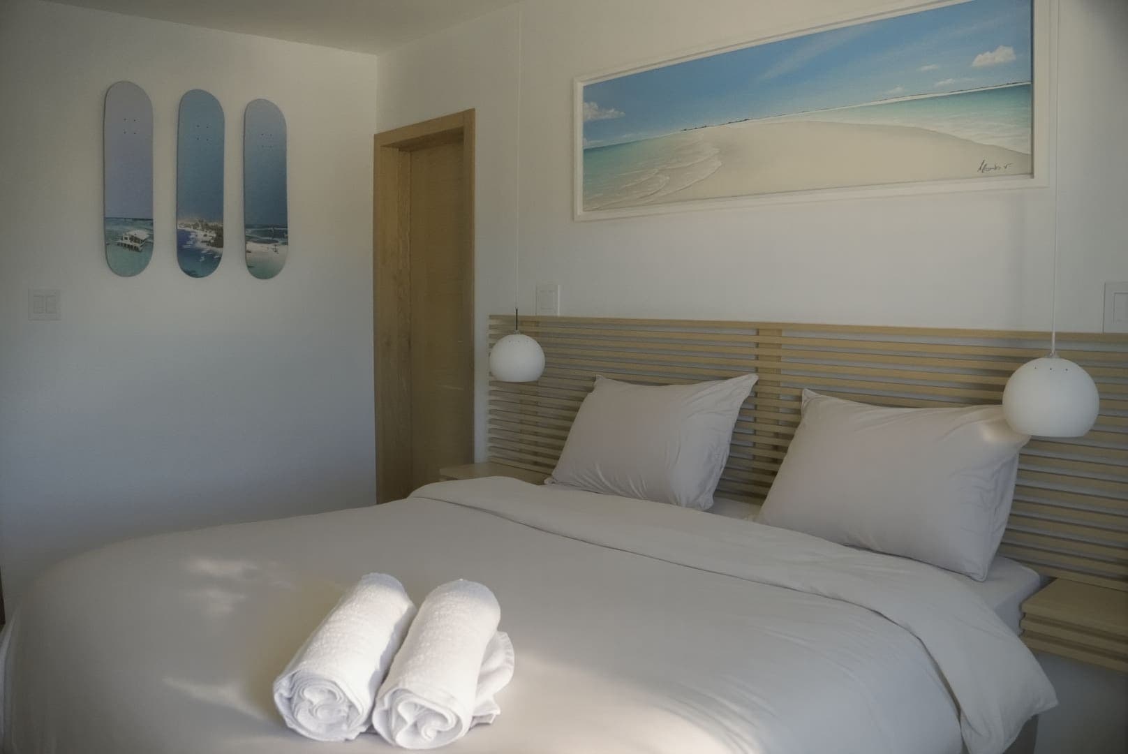 Habitación con cabecera de madera, lámparas de globo y un cuadro de la playa